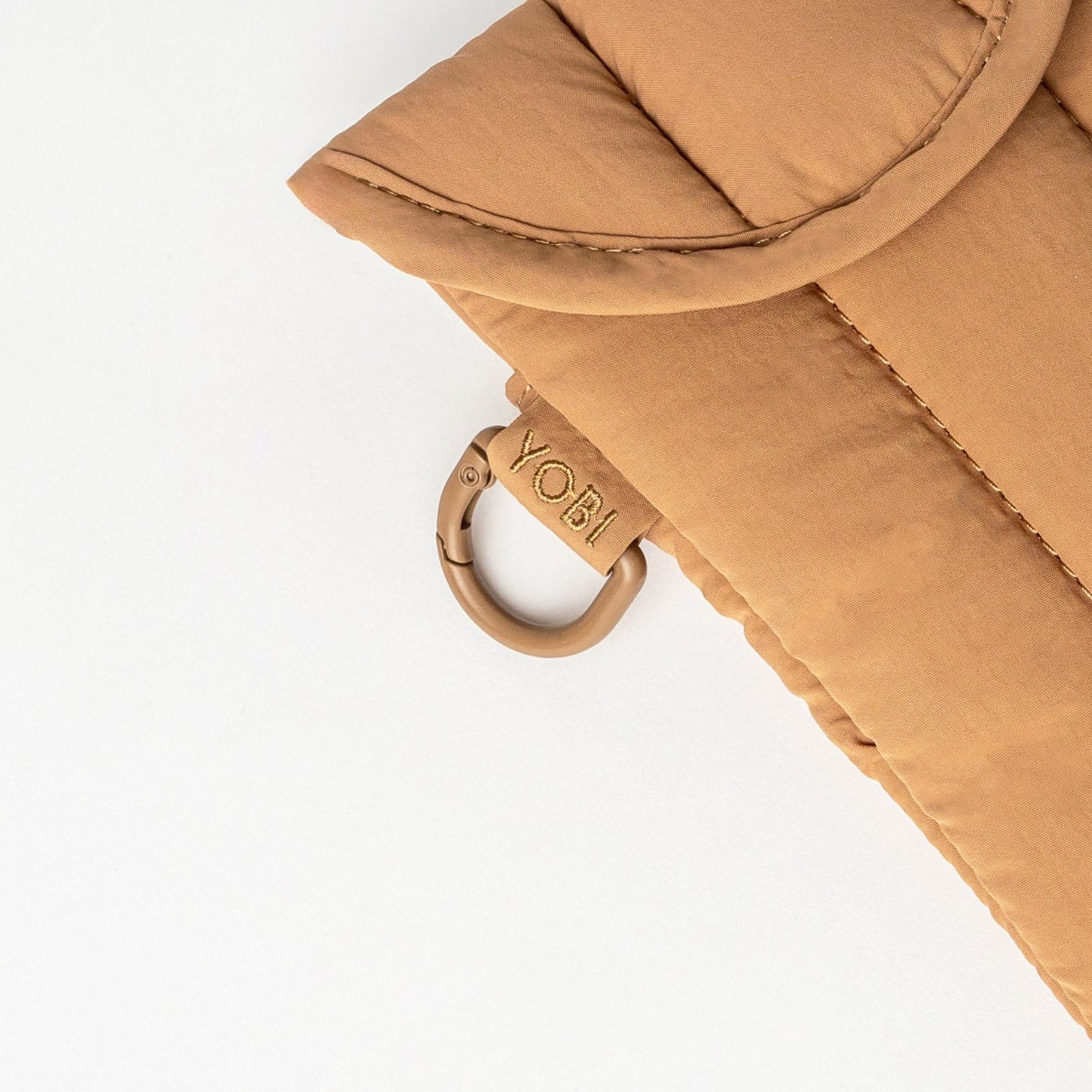 A tan quilted phone pouch with a flap closure and a small metal ring, photographed on a clean white background.
