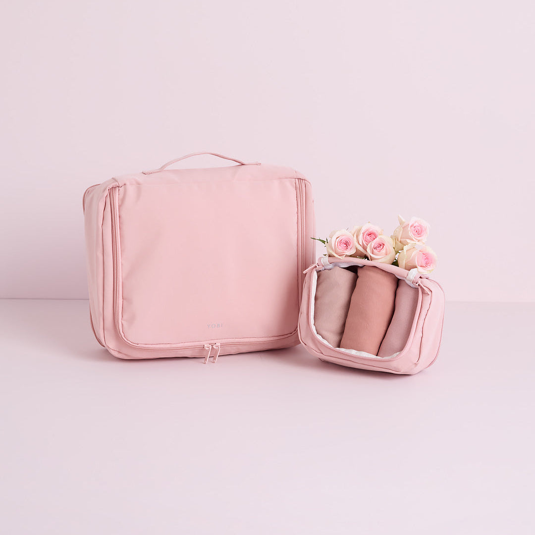 Pink travel bag with a smaller pink pouch containing pink items on a light pink background