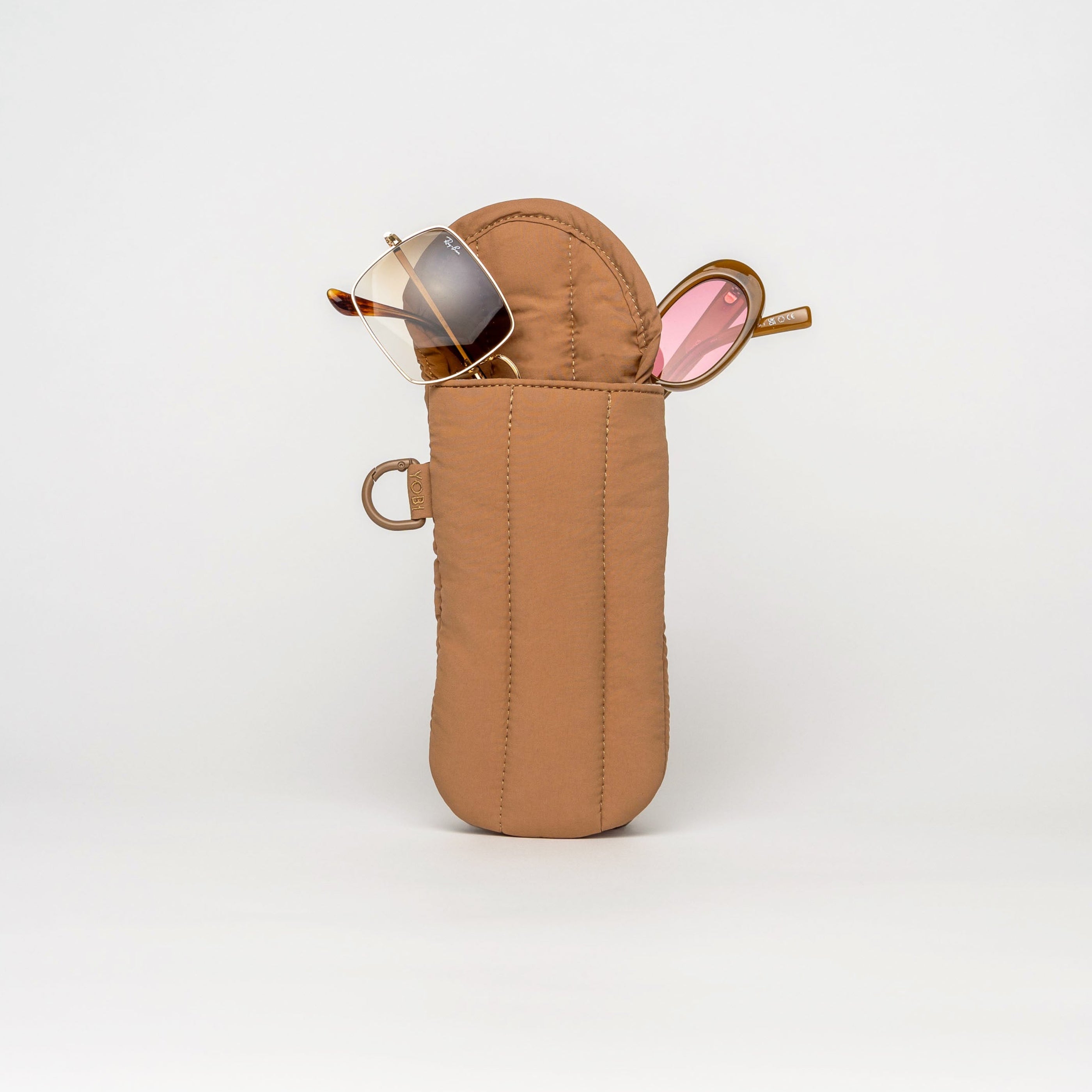 A tan nylon eyeglasses case standing upright on a white studio background, with a pair of sunglasses resting inside the open top.
