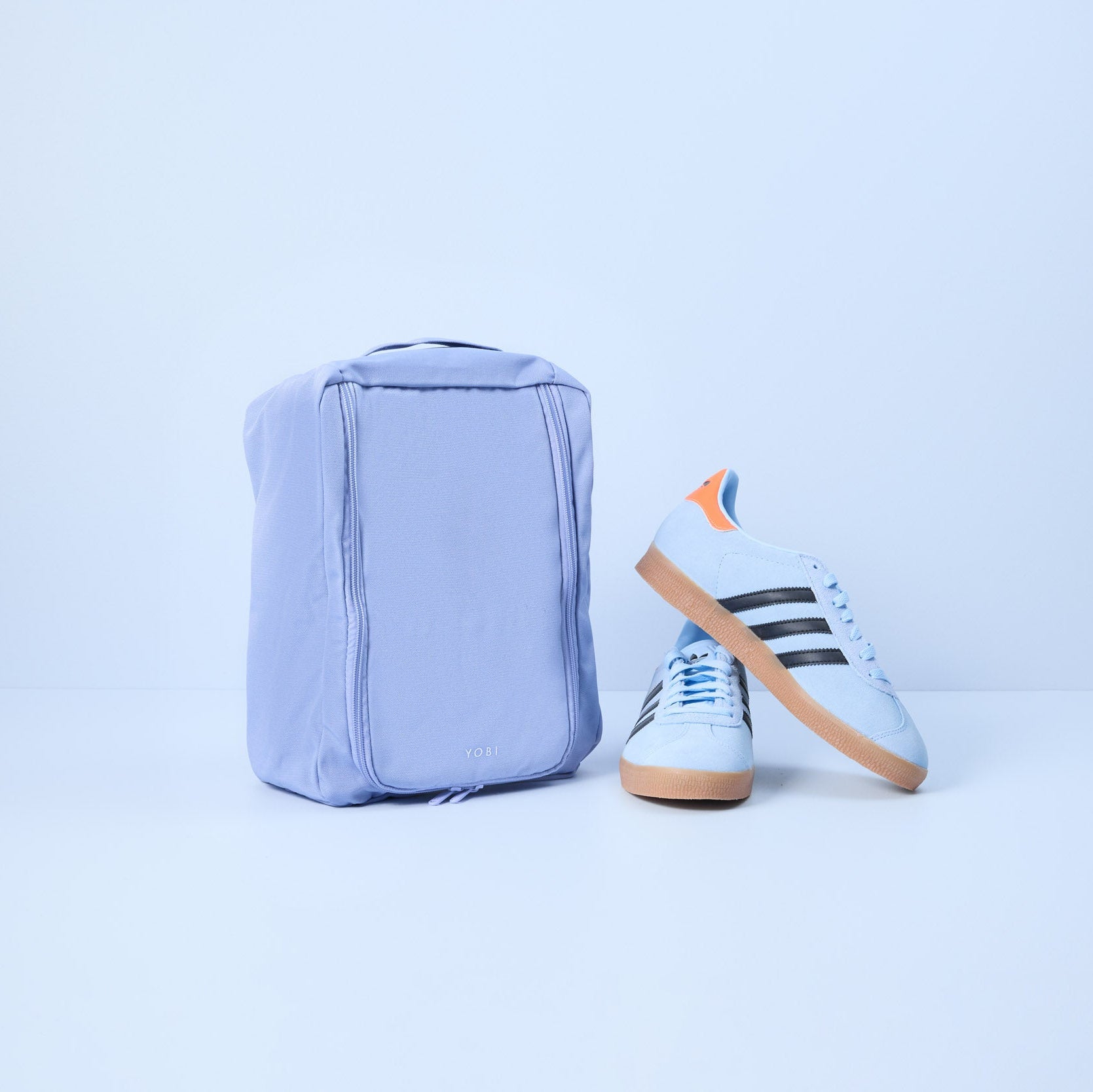 Light blue shoe bag and blue sneaker with orange accents on a light gray background